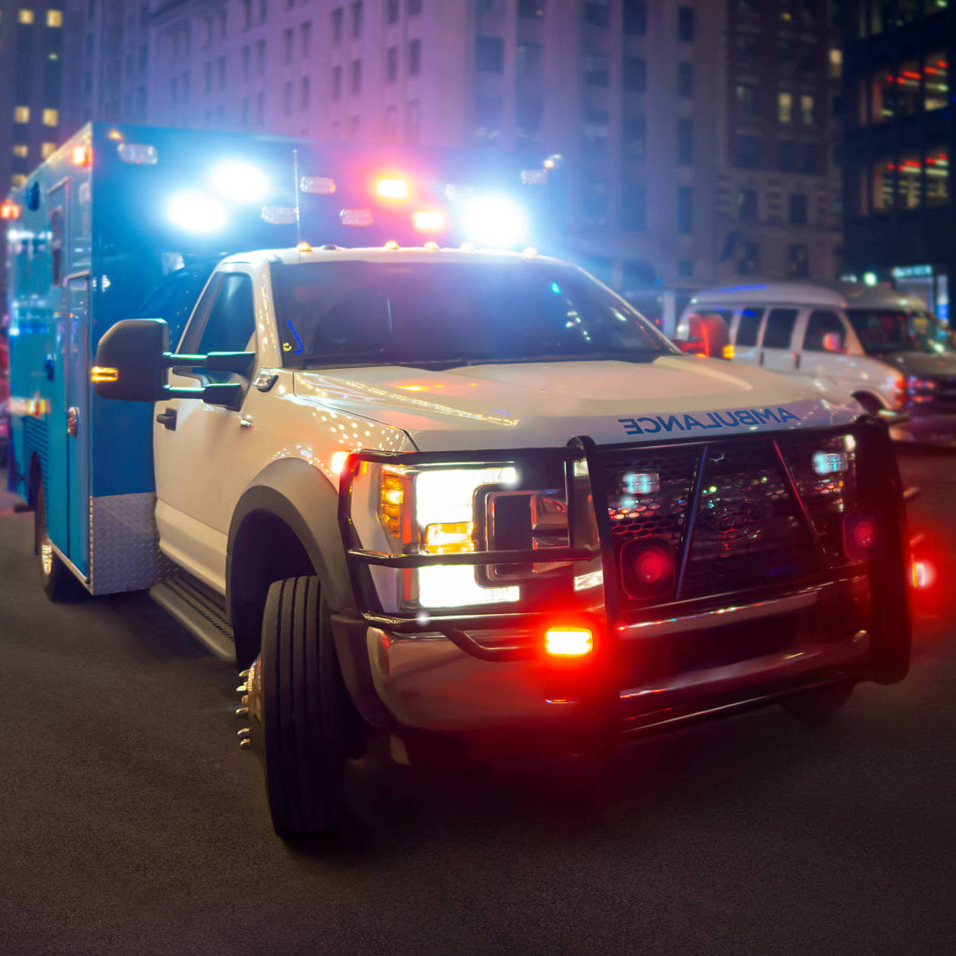 First Responder Ambulance On Urban City Street With Lights Flashing At Night